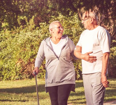 Mature caucasian female patient with a cane, taking a walk in a park while holding her husband